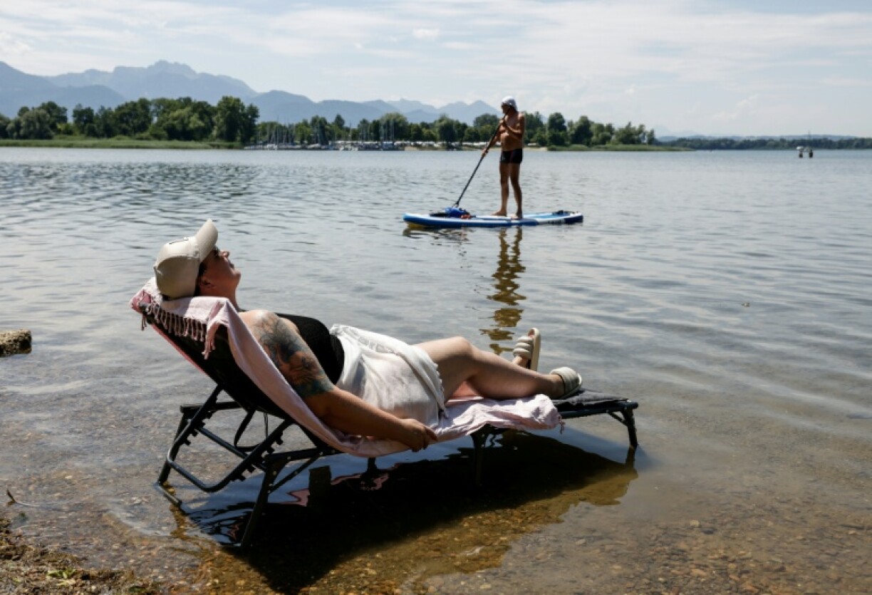 A woman puts her deck chair in the water at a beach at the Bavarian lake Chiemsee, where temperatures reaches some 32 degrees celsius on July 2, 2025