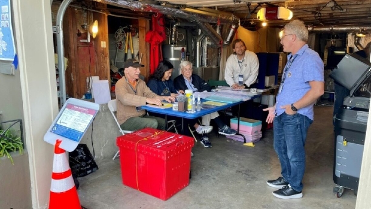 Michel Weksler (debout), président du bureau de vote installé dans le garage d'Angelo Figone (assis, à gauche), parle avec les agents électoraux en attendant les électeurs à San Francisco le 5 novembre 2024