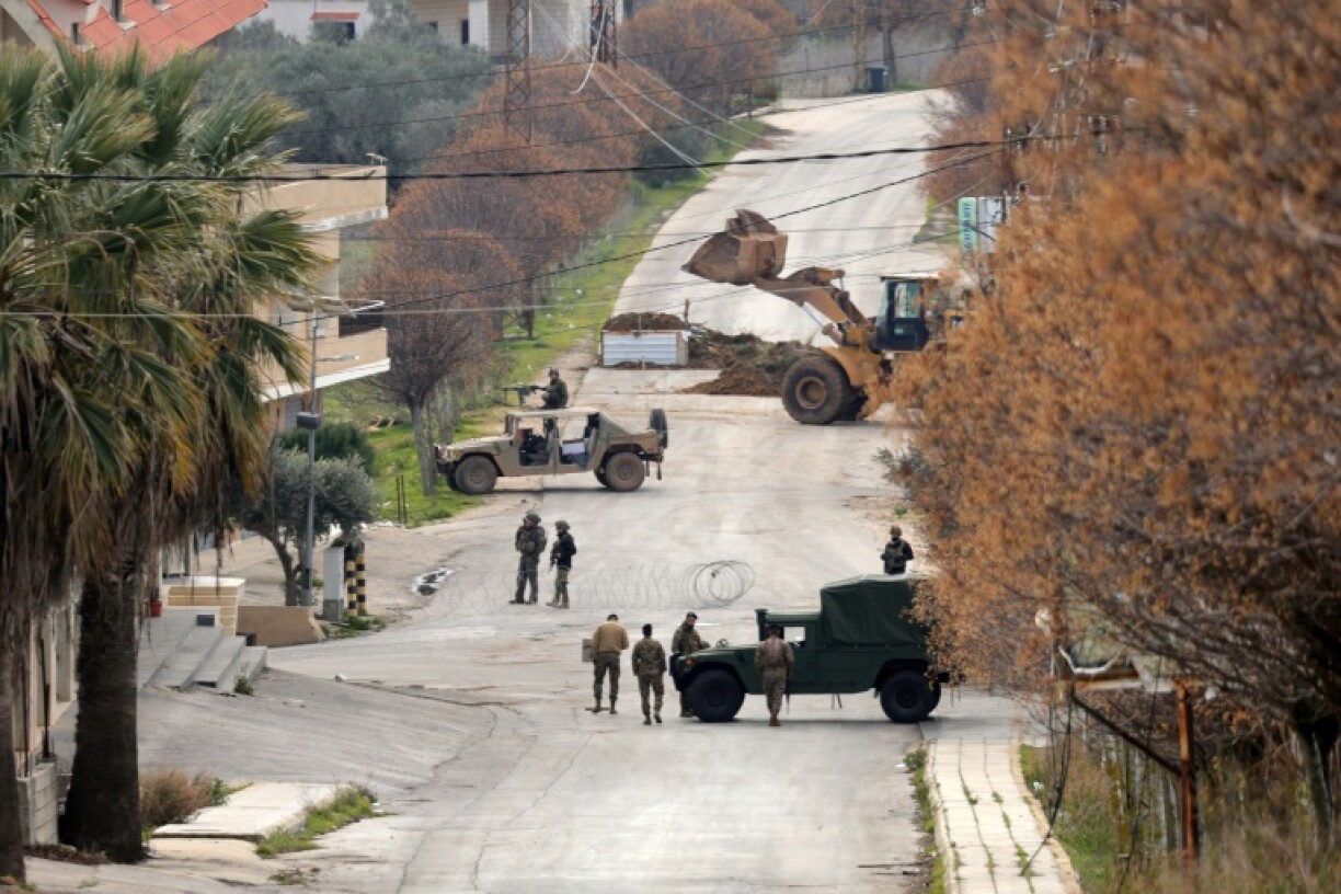 Lebanese army soldiers (R) and Israeli troops gather near their vehicles on either side of a barbed wire barrier, as an Israeli bulldozer pours soil to build a roadblock in Borj al-Mlouk in the border district of Marjayoun, southern Lebanon