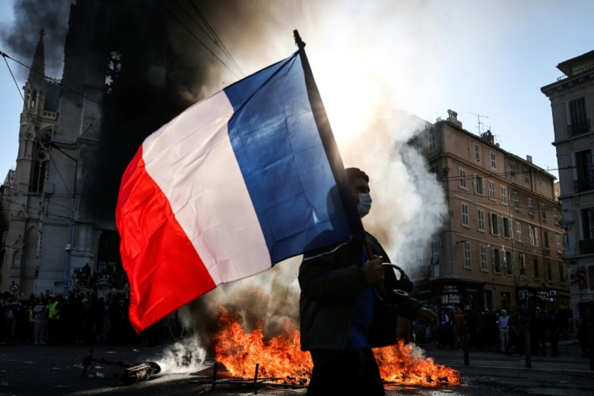 Un manifestant avec un drapeau français devant un feu, le 17 octobre 2026 à Marseille