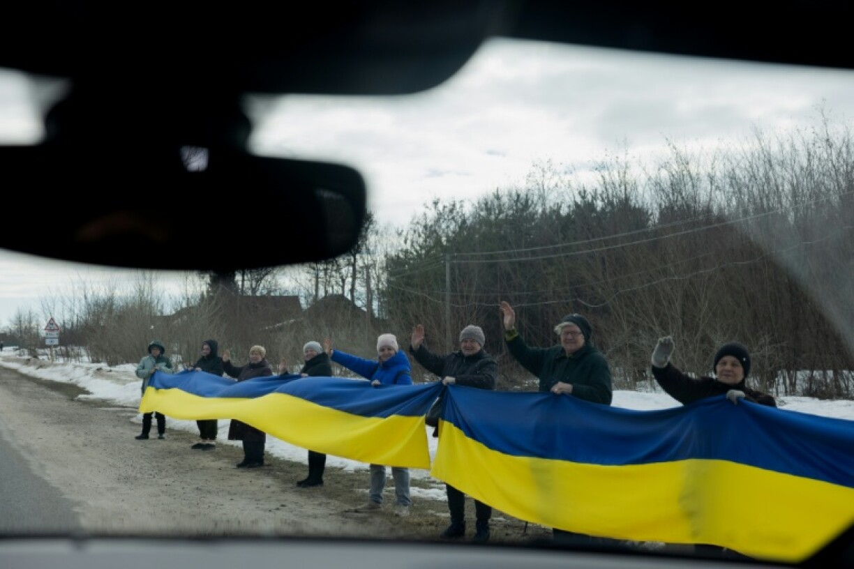 Des personnes tiennent un drapeau ukrainien le long d'une route pour accueillir un convoi de soldats libérés par les Russes après un échange de prisonniers, le 6 mars 2026 dans un lieu non précisé dans le nord de l'Ukraine