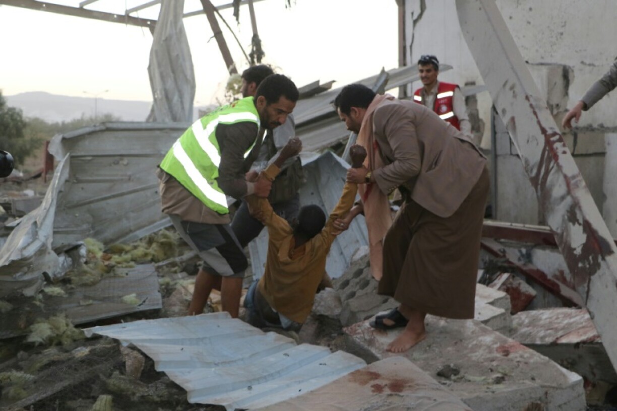 Yemeni rescuers pull an injured man from the rubble of the destroyed migrant centre