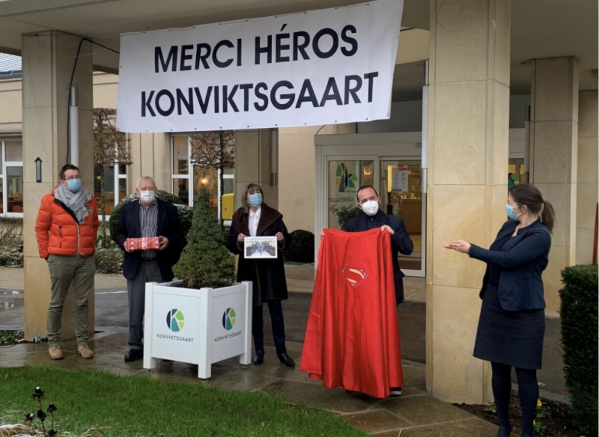 Marcello Loguercio, director of the Konviktsgaart, is being presented with a red superhero cape to honour his personnel, in the presence of Lydie Polfer, Luxembourg City mayor, and Maurice Bauer, the alderman responsible for social affairs.