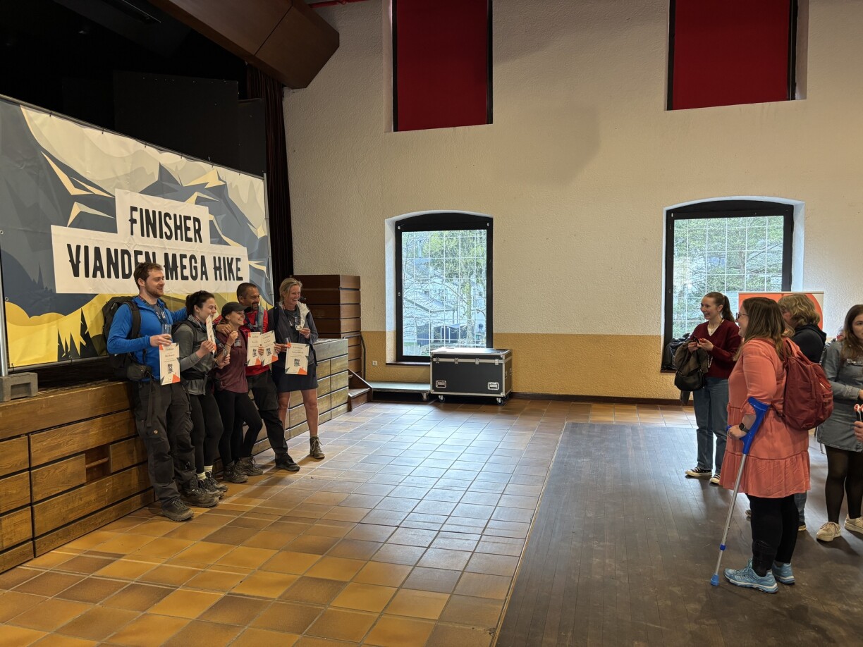 Endlech ukomm an der Larei: eng Foto virum Finisher-Plakat mat Certificat am Grapp a Medail ëm den Hals.