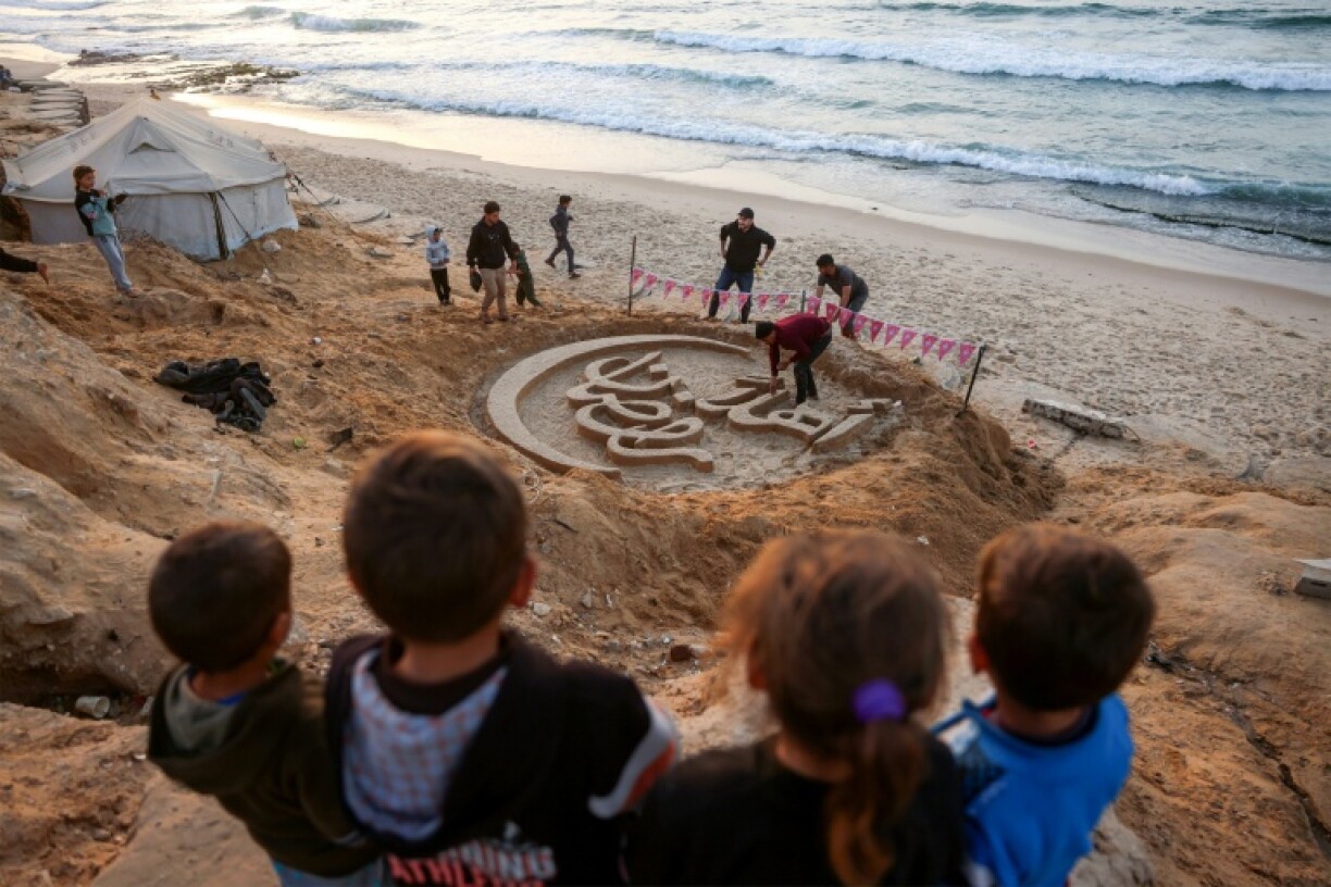 Des enfants regardent une sculpture de sable proclamant
