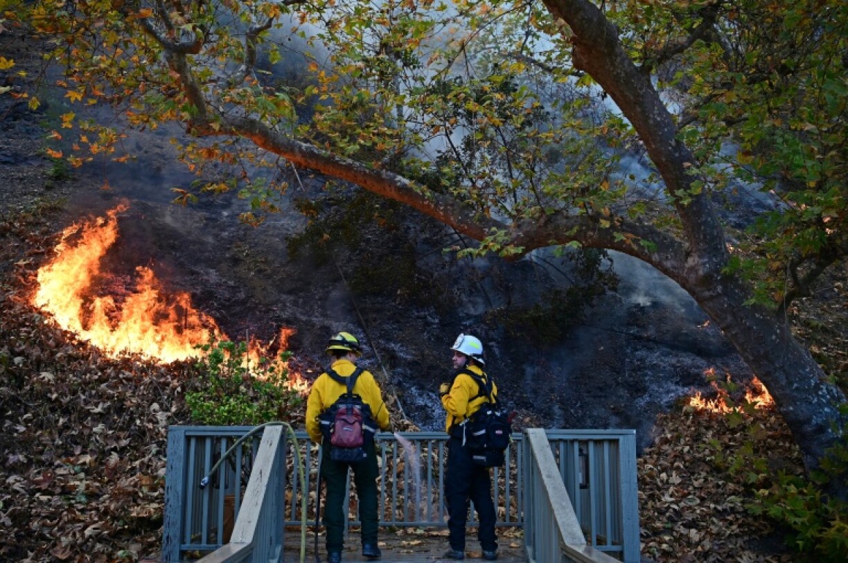 Firefighters work to put out flames behind a home in the Mandeville Canyon neighborhood of Los Angeles
