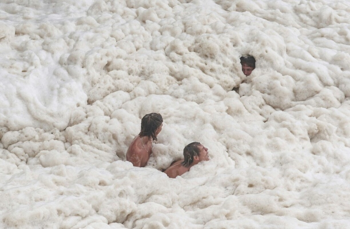 Young men play in sea foam created by record-breaking waves in Coolangatta
