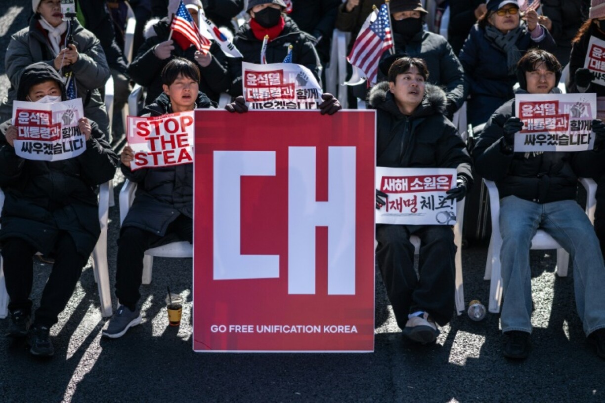 Demonstrators sit beside a board that reads
