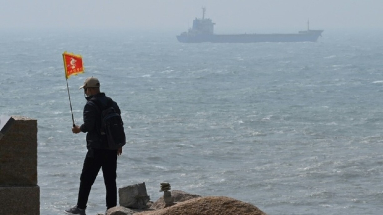 Un homme marche, un drapeau à la main, alors qu'un navire croise au large de Pingtan, sur la côte chinoise, au point géographique le plus proche de Taïwan, le 8 avril 2023