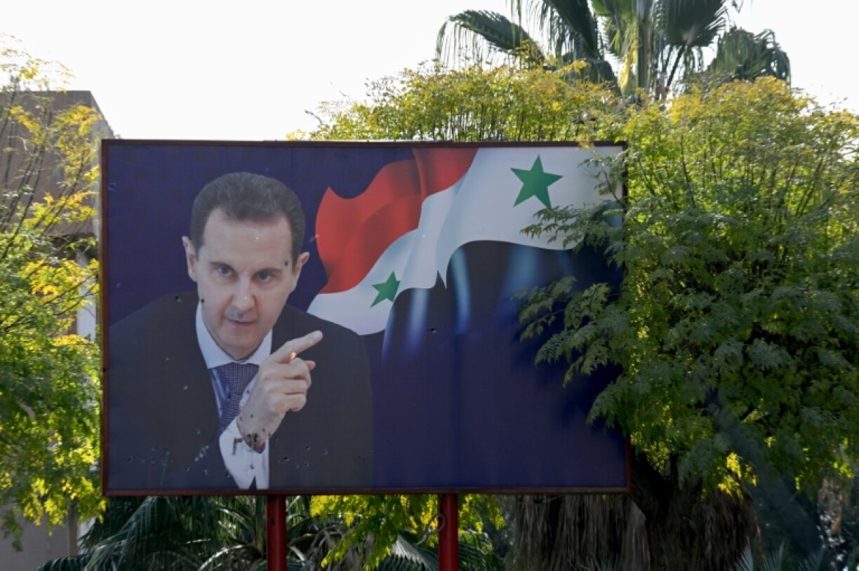 A portrait of ousted Syrian president Bashar al-Assad next to a national flag is slightly damaged by shrapnel outside the Barzeh scientific research centre north of the Syrian capital Damascus, after being targeted by a December 2024 Israeli airstrike