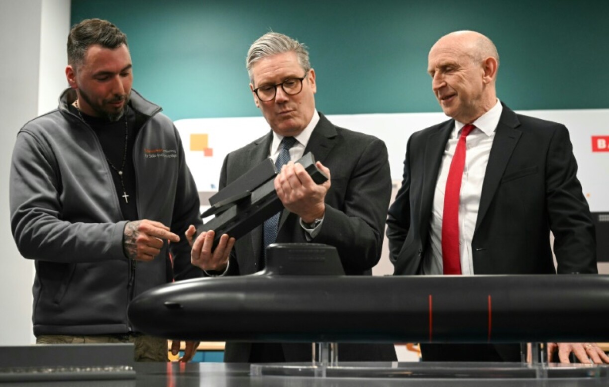 Britain's Prime Minister Keir Starmer (C) and Defence Secretary John Healey (R) are shown a submarine model while visiting BAE system apprentices in northwestern England