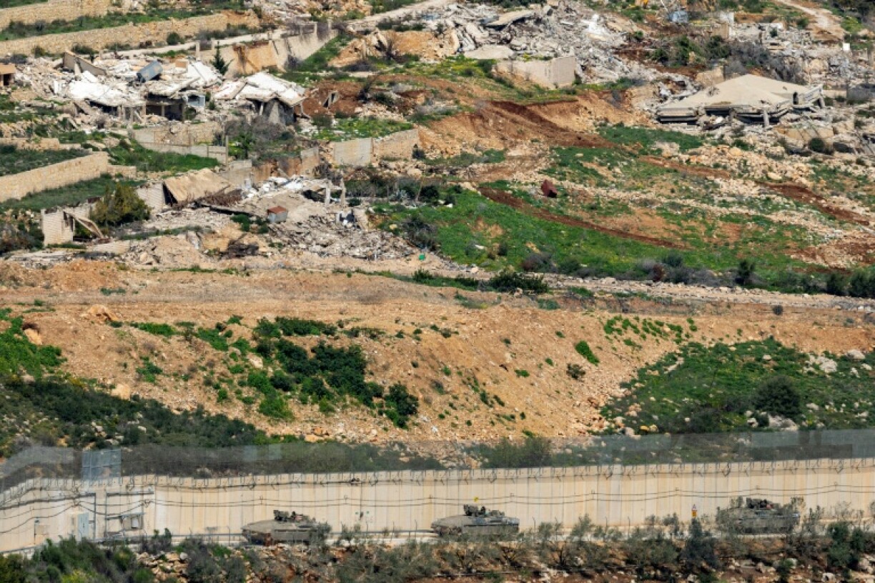 Des véhicules de combat de l'armée israélienne manœuvrent du côté israélien de la clôture frontalière, en face d'un village libanais détruit, vu de la Haute Galilée, dans le nord d'Israël, le 16 mars 2026