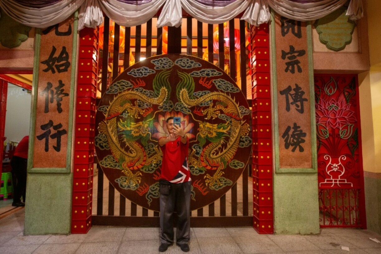 A man uses his mobile phone to take a selfie in front of a temple in the Chinatown area of Bangkok, Thailand
