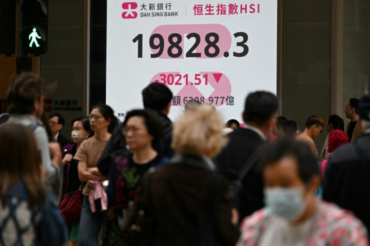 Pedestrians walk past an electronic sign board showing the closing price of the Heng Seng Index on April 7, 2025