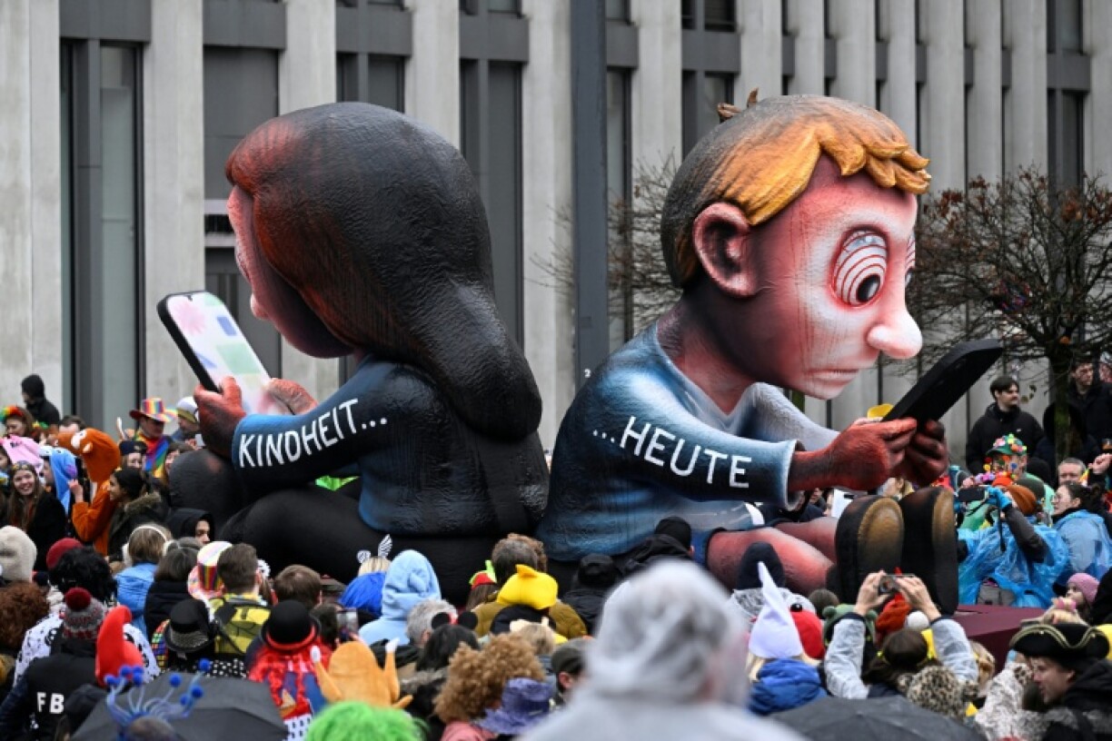A carnival float designed by German carnival float builder Jacques Tilly featuring children looking at their phones and a text reading 'Childhood' (L) and 'Today' (R) is pictured during the parade to celebrate Rose Monday (Rosenmontag), on February 16, 2026 in Duesseldorf, western Germany.