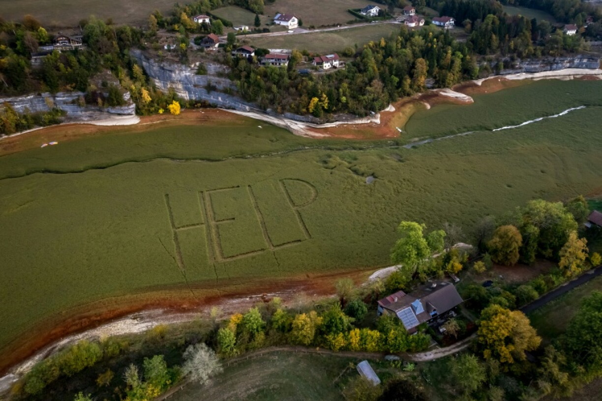 Cette photographie aérienne montre un gigantesque « Help » écrit par des habitants sur le lit herbeux de l’ancien lac asséché des Brenets (Lac des Brenets), partie du Doubs qui forme une frontière naturelle entre l’est de la France et l’ouest de la Suisse, aux Brenets, le 1er octobre 2026