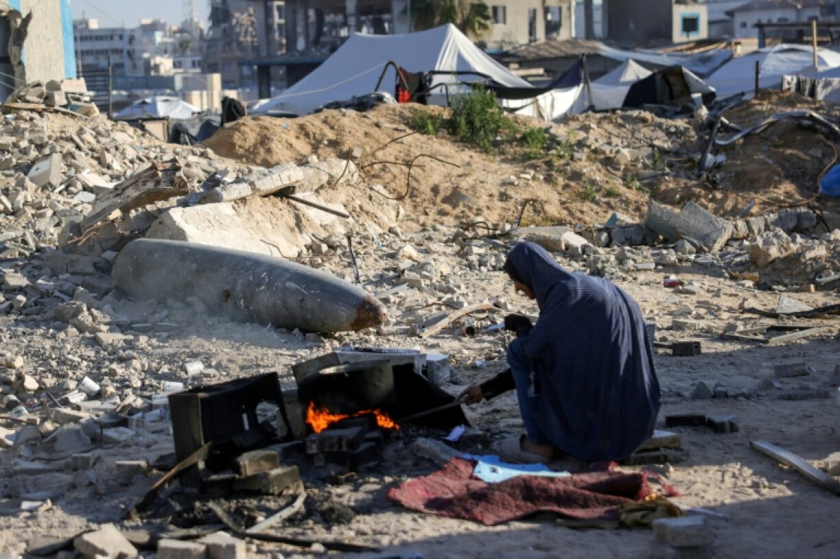 A displaced Palestinian woman cooks near unexploded ordnance in Gaza City