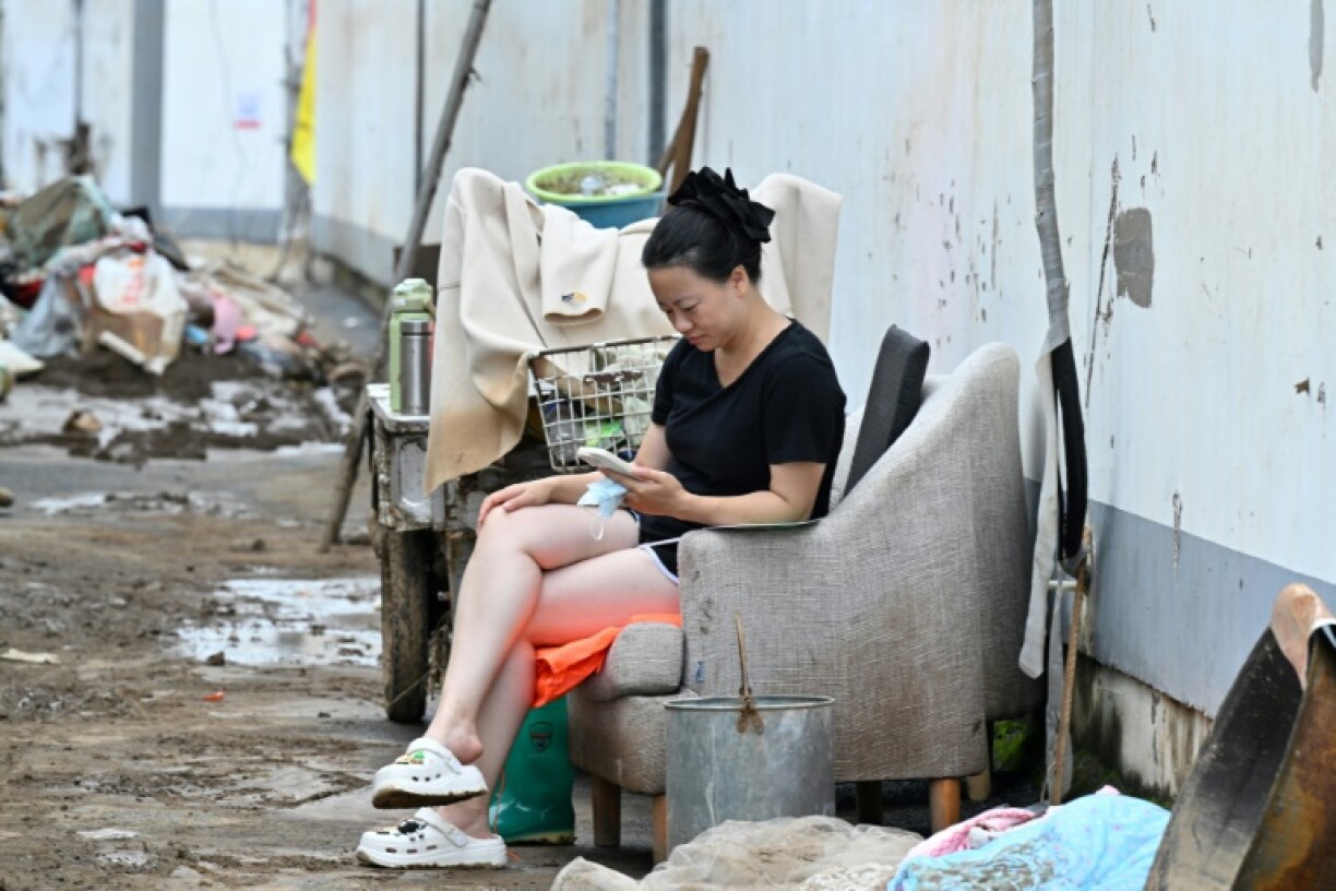 A resident seated on a couch checks her mobile phone while cleaning her house following deadly flooding in Taishitun village, Miyun district, Beijing on August 5, 2025