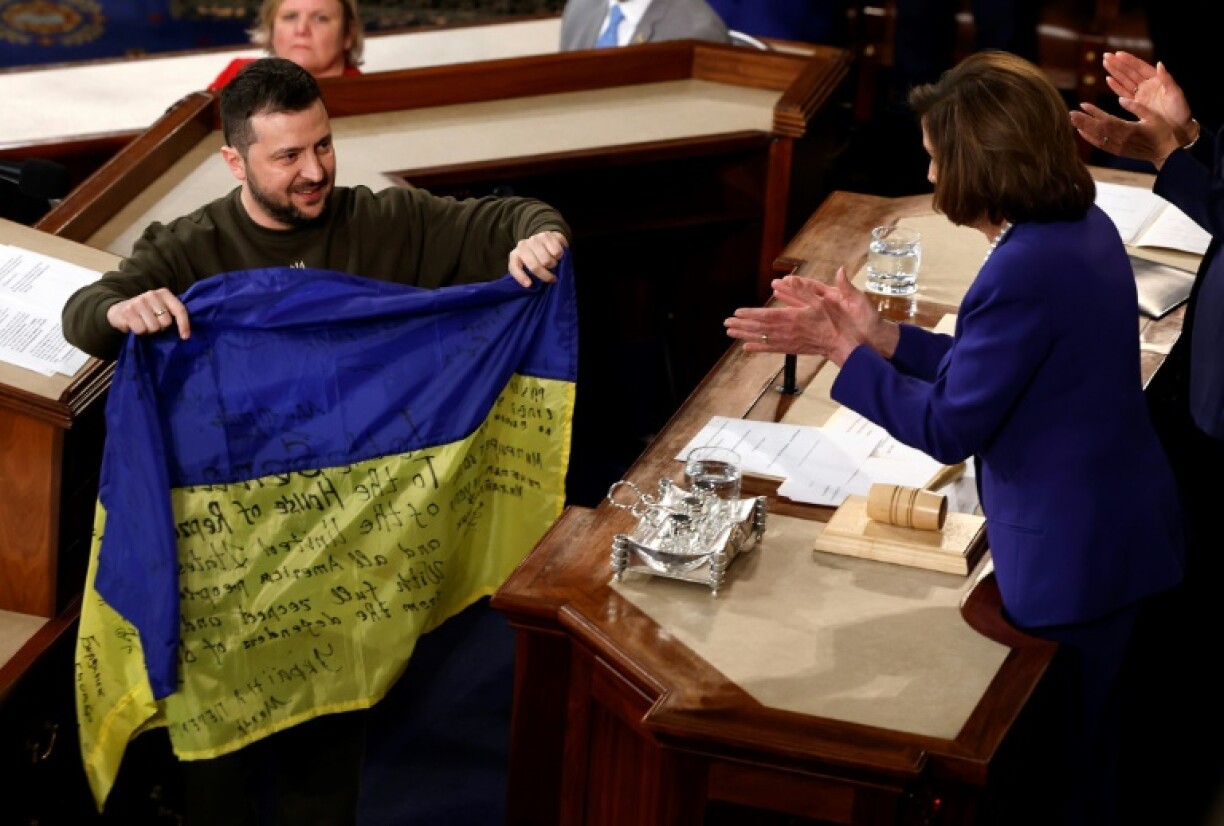 Le président ukrainien Volodymyr Zelensky (g) remet un drapeau de son pays à la présidente de la Chambre des représentants Nancy Pelosi après son discours devant le Congrès américain, le 21 décembre 2022 à Washington