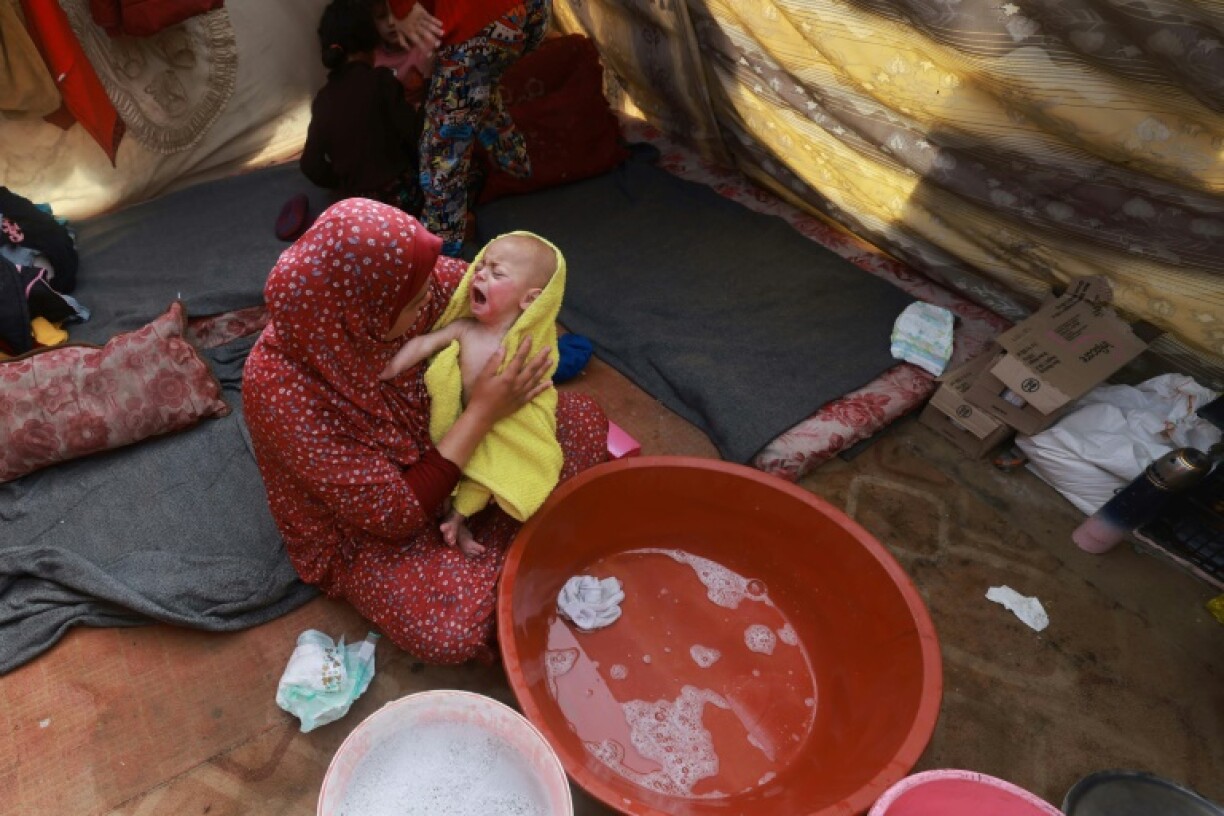 Une femme sèche un bébé après lui avoir donné un bain, dans une tente d'un camp de déplacés palestiniens à Rafah, dans le sud de la bande de Gaza, le 18 janvier 2024