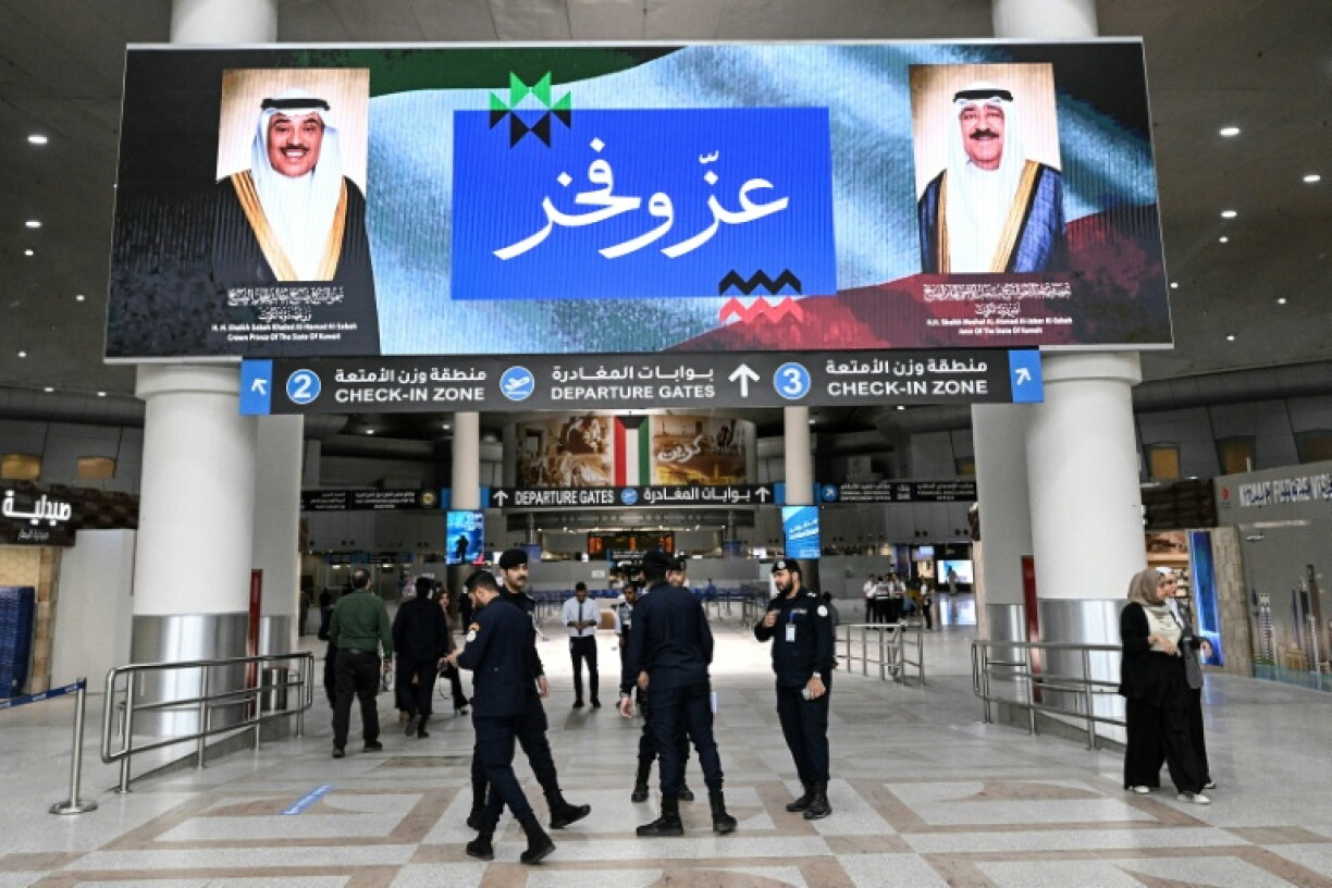 Des agents de sécurité koweïtiens sous un écran affichant les portraits de l'émir du Koweït, le cheikh Mech'al al-Ahmad al-Jaber al-Sabah (à droite), et du prince héritier koweïtien, le cheikh Sabah al-Khaled al-Hamad al-Sabah, accompagnés des mots