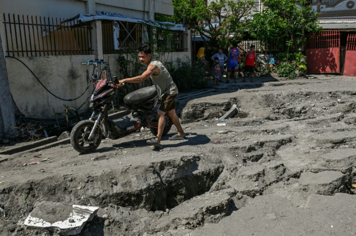 Un habitant pousse sa moto sur une route endommagée après un séisme de magnitude 7,8 à General Santos, le 9 juin 2026 aux Philippines
