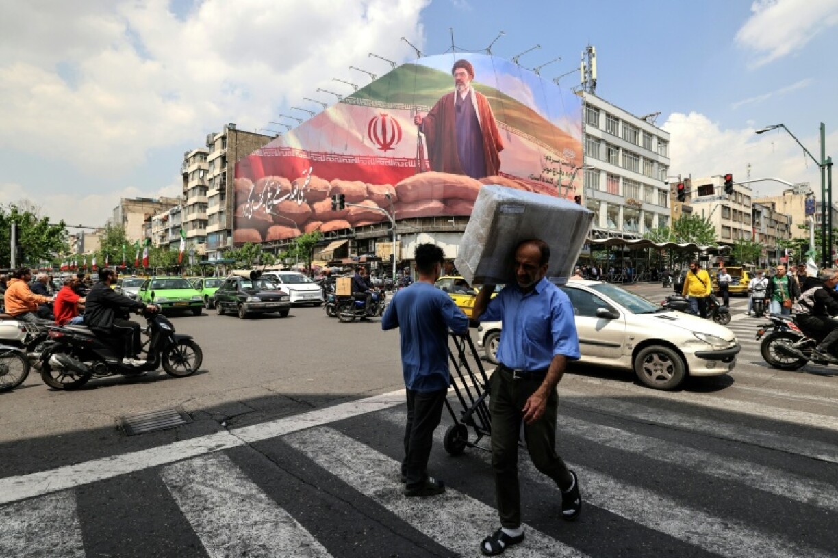 Des passants marchent devant un grand panneau représentant le guide suprême iranien Mojtaba Khamenei, le 20 avril 2026 à Téhéran