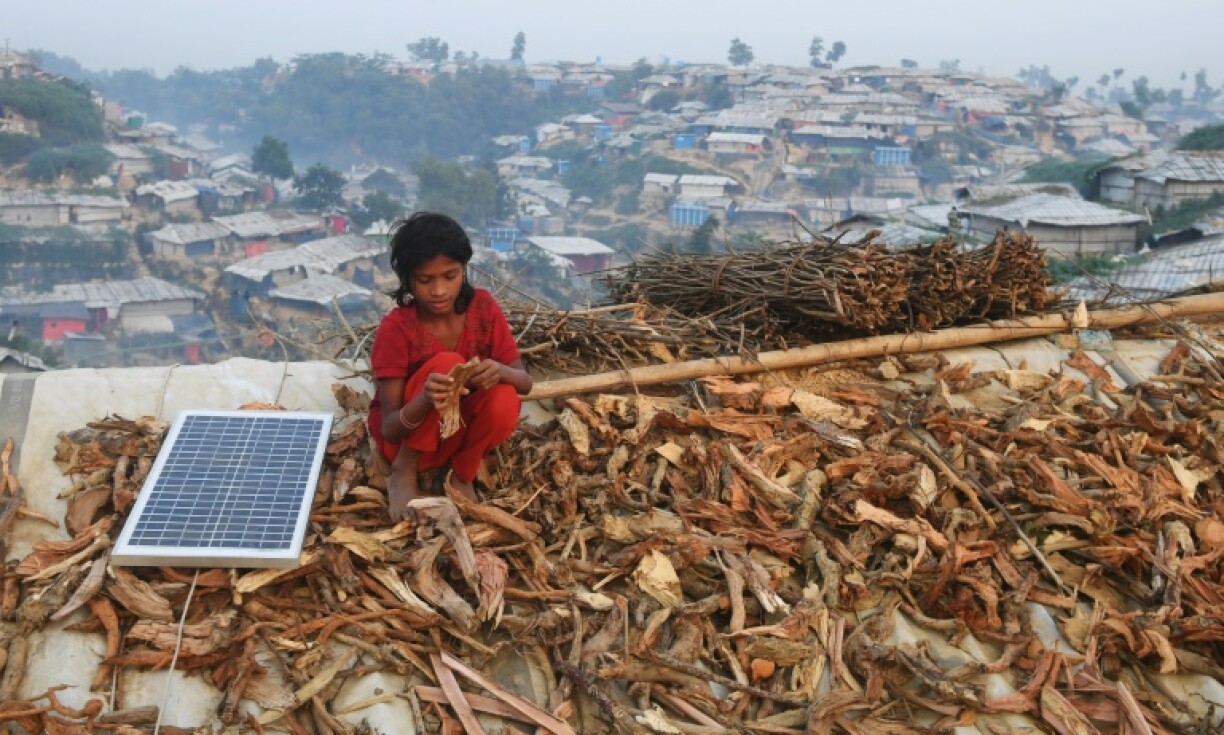 A young Rohingya refugee spreads out fire wood for drying on the roof of a shack, next to a solar panel, in Bangladesh's Cox's Bazar in 2018