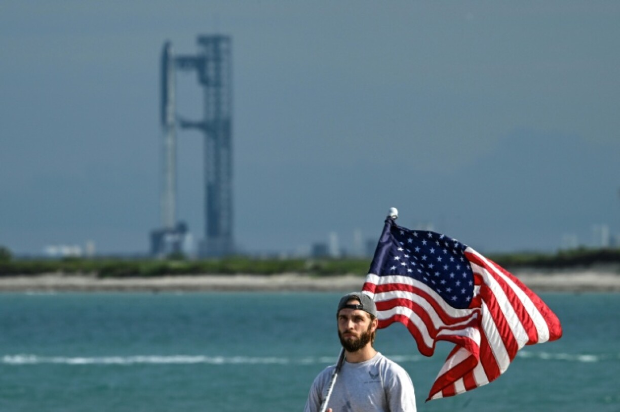 A man with a US flag walks in front of the massive rocket