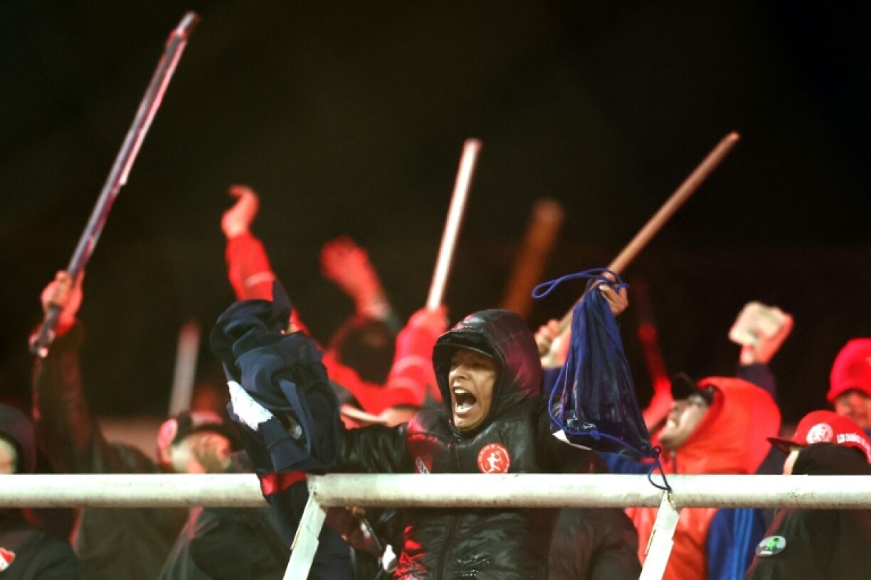 Independiente fans display stolen clothing and brandish sticks at the stands where Universidad de Chile fans were sitting