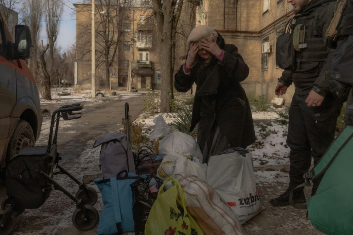An elderly woman stands next to her belongings before boarding a minivan to be evacuated by volunteers and members of the Ukrainian police
