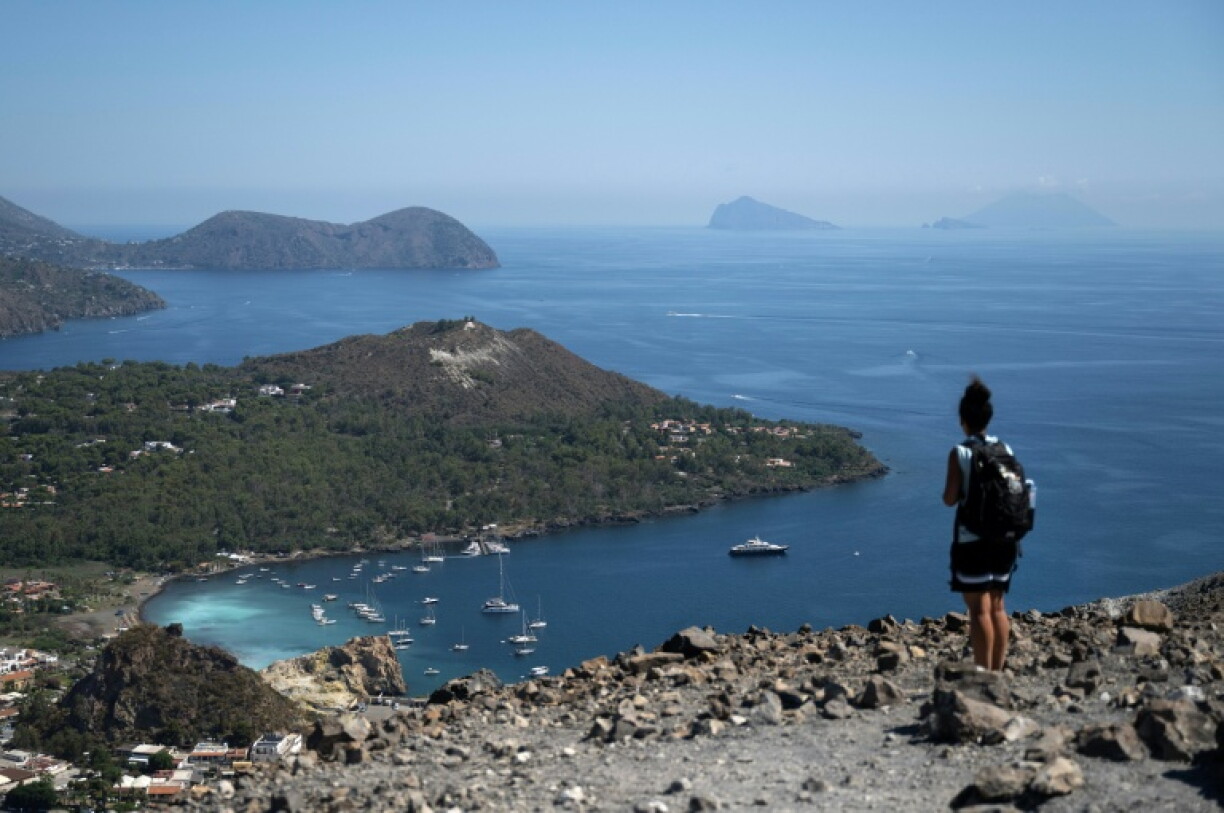 Une touriste sur le bord du cratère de La Fossa, sur l'île de Vulcano, avec (g-d) les îles de Lipari, Panarea et Stromboli, dans l'archipel des Éoliennes, au large de la Sicile, le 9 juillet 2026 en Italie