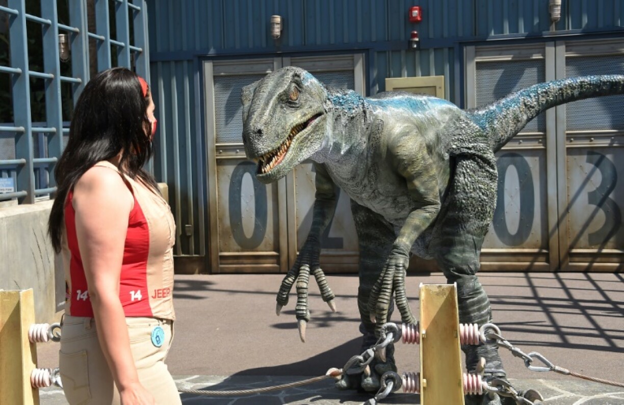 Une visiteuse du parc d'attractions Universal Studios de Los Angeles passe devant une mascotte déguisée en vélociraptor, le 15 avril 2021