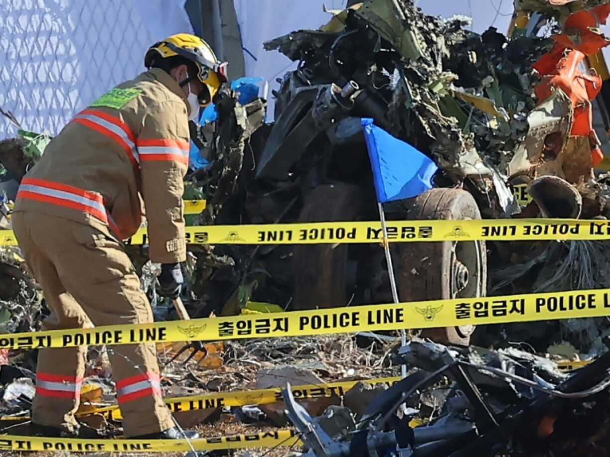 A firefighter works near wrecked landing gear at the scene where a Jeju Air Boeing 737-800 series aircraft crashed and burst into flames at Muan International Airport