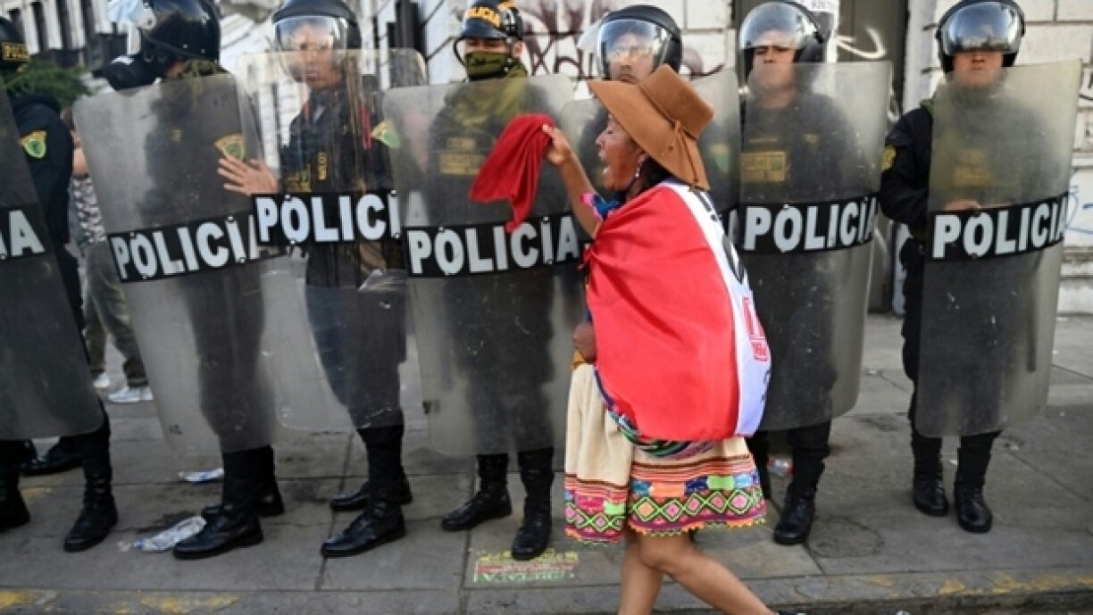 Une femme indigène passe devant des policiers anti-émeute au cours d'une manifestation réclamant la démission de la président du Pérou, Dina Boluarte, le 23 janvier 2023 à Lima