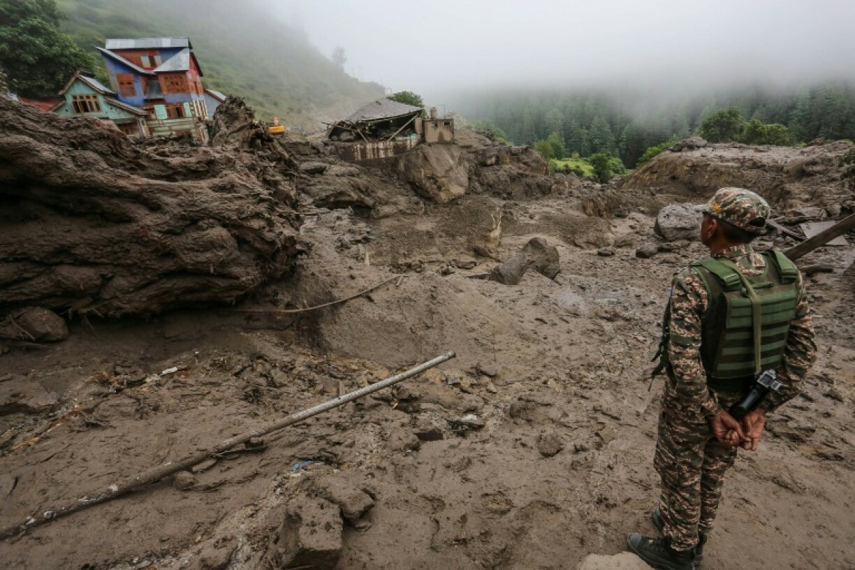 An Indian security officer stands near damaged houses at the site of a flash flood at a village in Indian-administered Kashmir's Kishtwar district