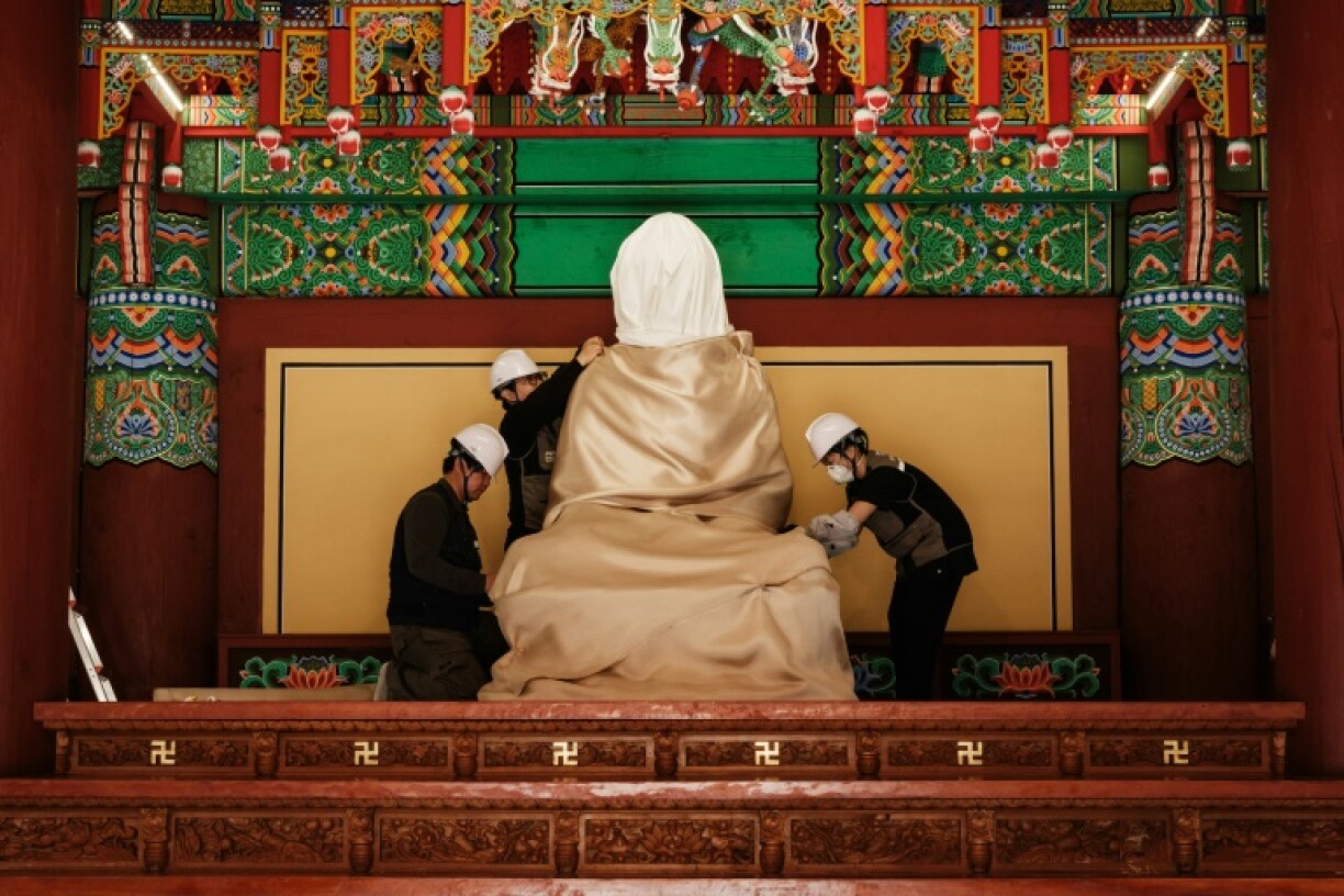 Members of the Gyeongbuk Seobu Cultural Heritage Care Center wrap a Buddha statue with cotton cloth and a fire-retardant blanket after evacuating all other items from the Gounsa Temple in Uiseong