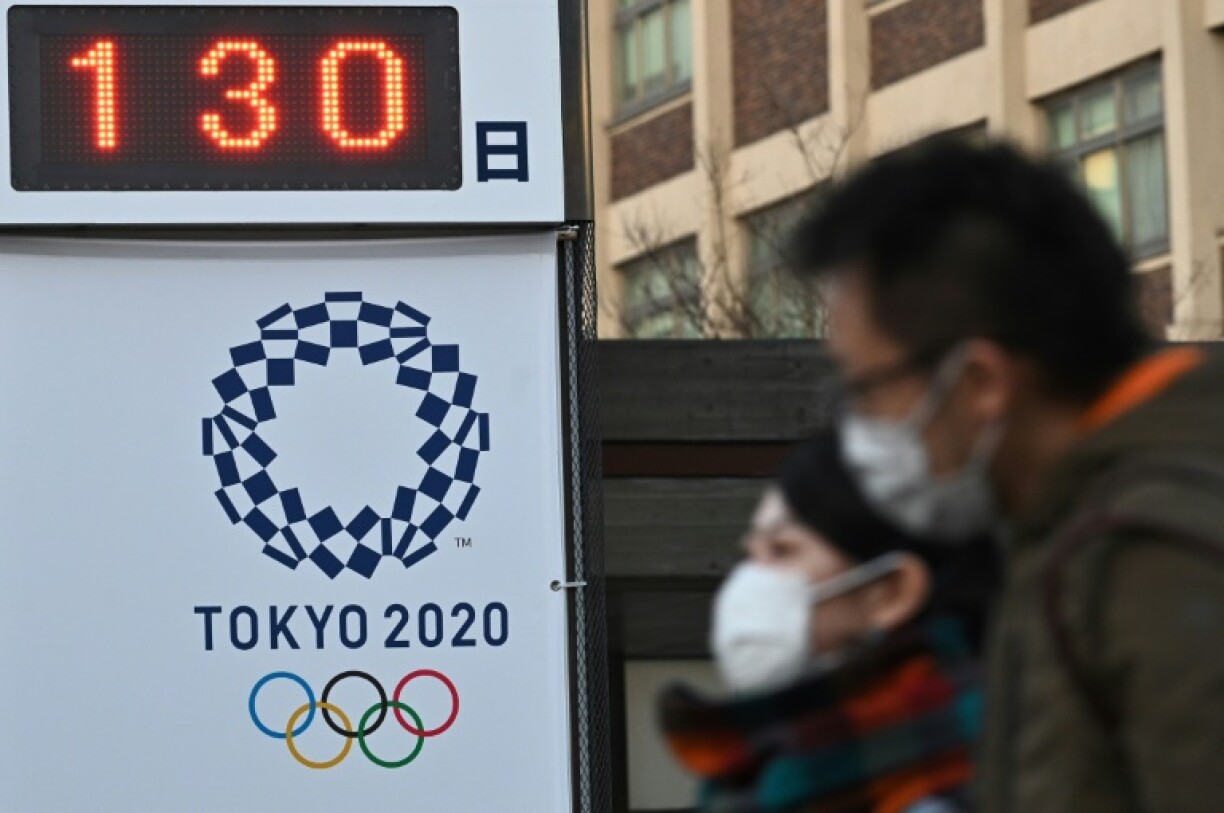 Des piétons portant un masque devant un panneau comptant les jours avant les Jeux olympiques de Tokyo, à Yokohama le 16 mars 2020