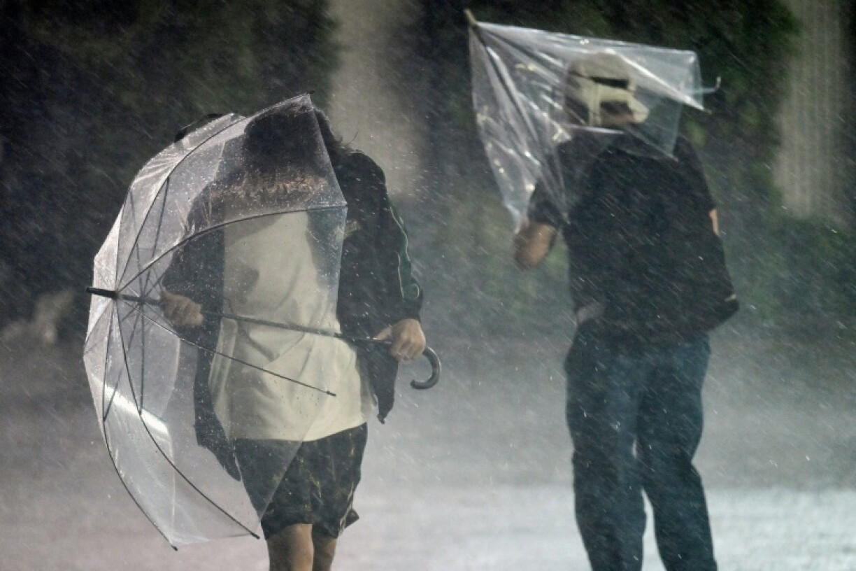 Des piétons retiennent leurs parapluies face à des vents violents et de fortes pluies à Chiba, à l'approche du typhon Dujuan, le 21 septembre 2026 au Japon
