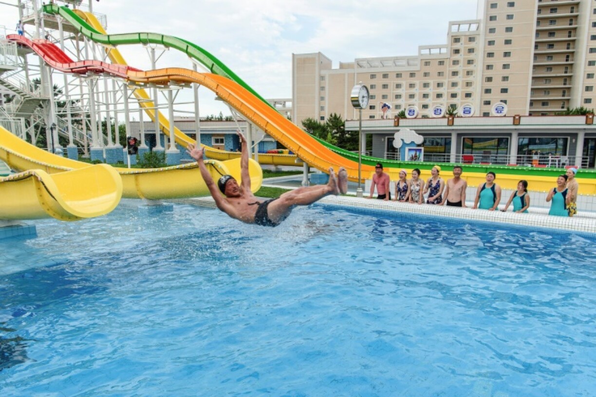 Domestic tourists watch as a man uses a slide into a swimming pool at the Myongsasimni Water Park in North Korea