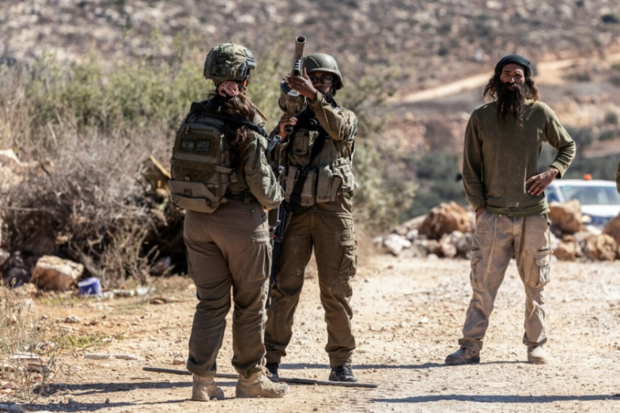 Israeli soldiers and an Israeli settler gather on a road close to an olive grove following a reported attack by settlers on a Palestinian home in the Israeli-occupied West Bank village of Turmus Ayya