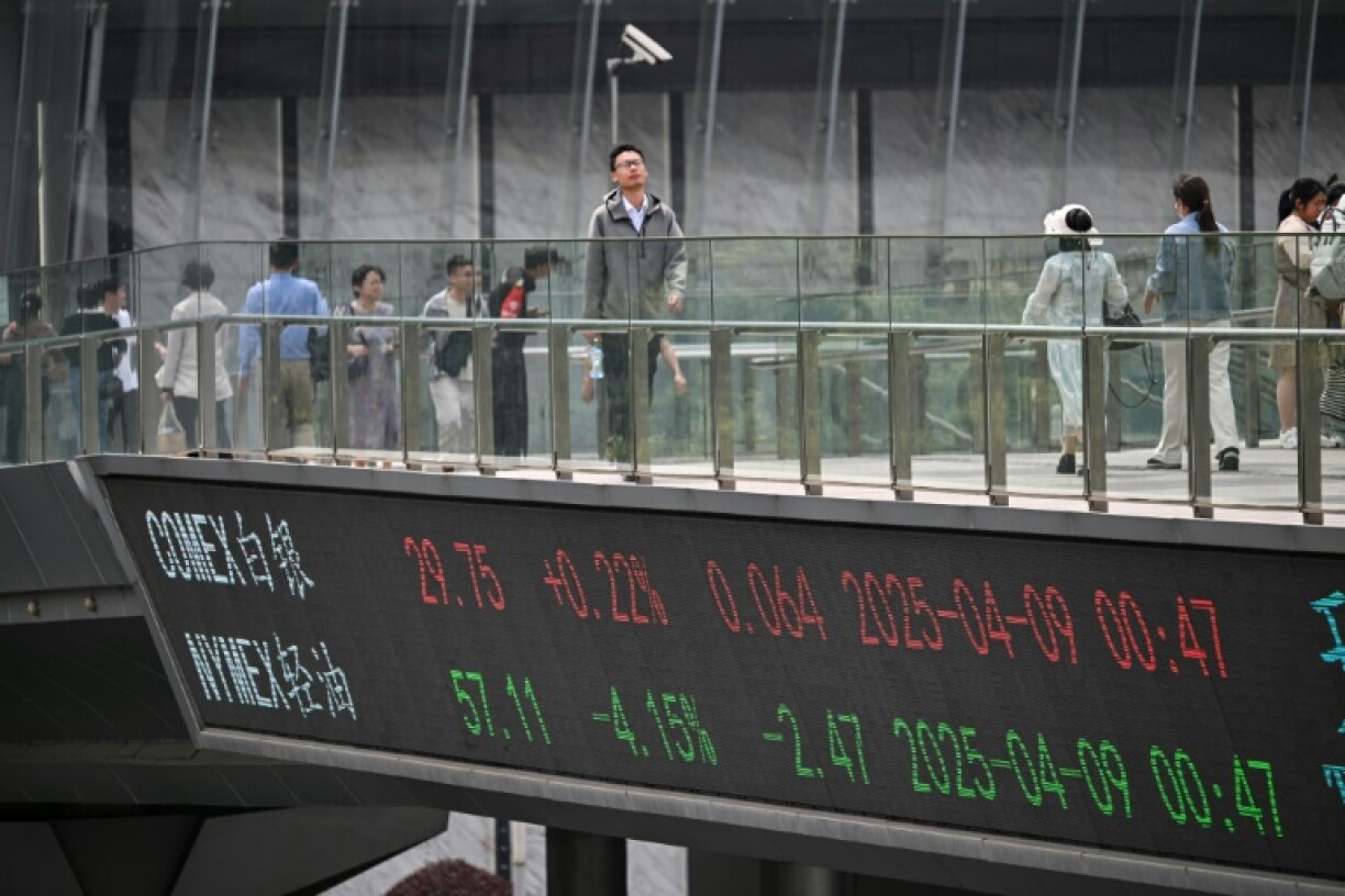 People walk across a foot bridge with a board showing financial market information in Shanghai