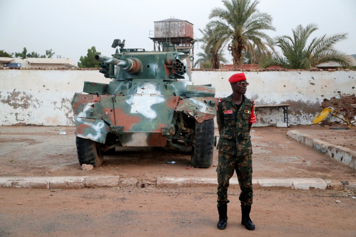 En Zaldot vun der sudaneesescher Arméi steet virun engem Panzer, deen am Krich beschiedegt gouf.
