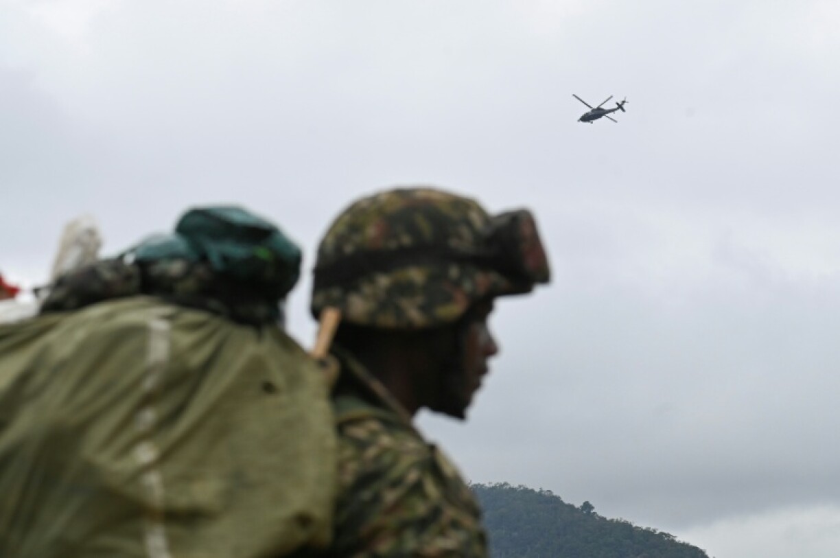 An Army helicopter flies overhead as soldiers gather their equipment to retreat