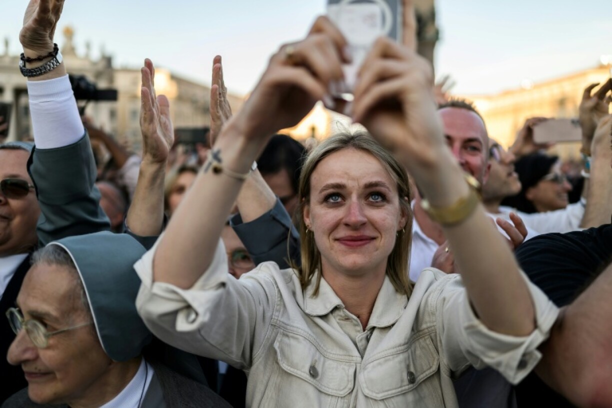 A woman uses her mobile phone to snap photos of the newly elected Pope Leo XIV at the Vatican, the first pope who assumes the role with a long social media history