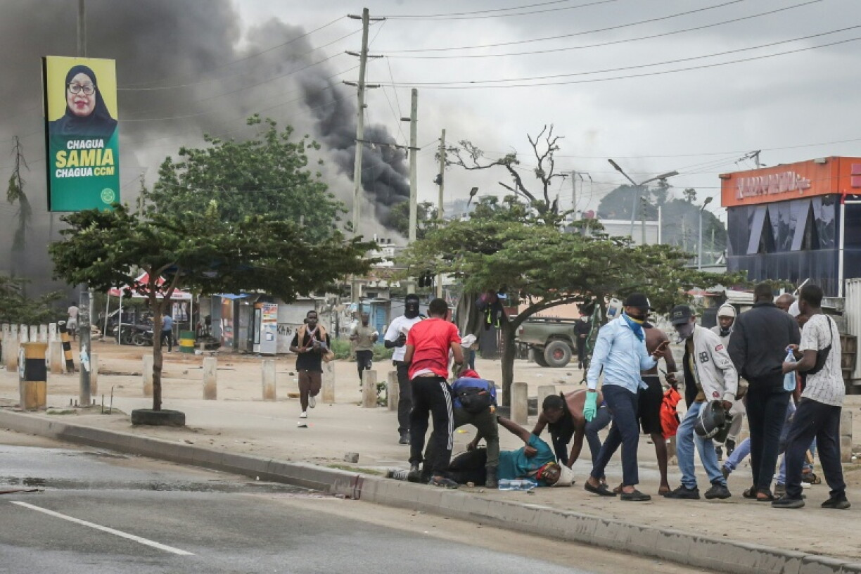 Des manifestants aident l'un d'entre eux, blessé, près de barricades en feu, le 29 octobre 2025 à Dar es Salaam, capitale économique de la Tanzanie