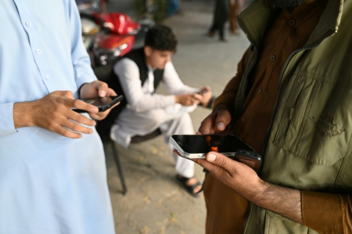 Jubilant Afghan men use their mobile phones in Kabul after mobile networks and the internet were restored across Afghanistan on October 1, 48 hours after the Taliban authorities shut down telecommunications