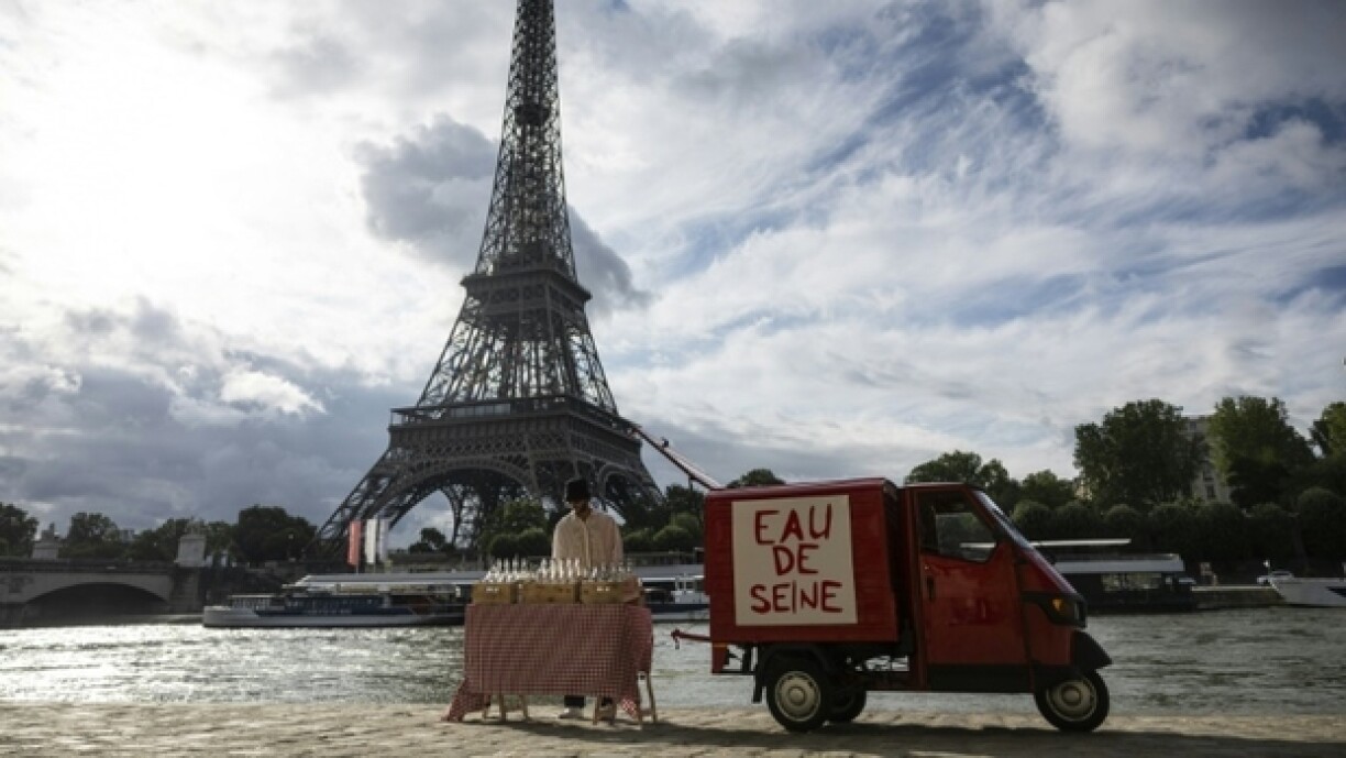 Un acolyte de l'artiste de rue James Colomina vend de l'eau en bouteille de la Seine devant la Tour Eiffel, à Paris le 10 juillet 2024