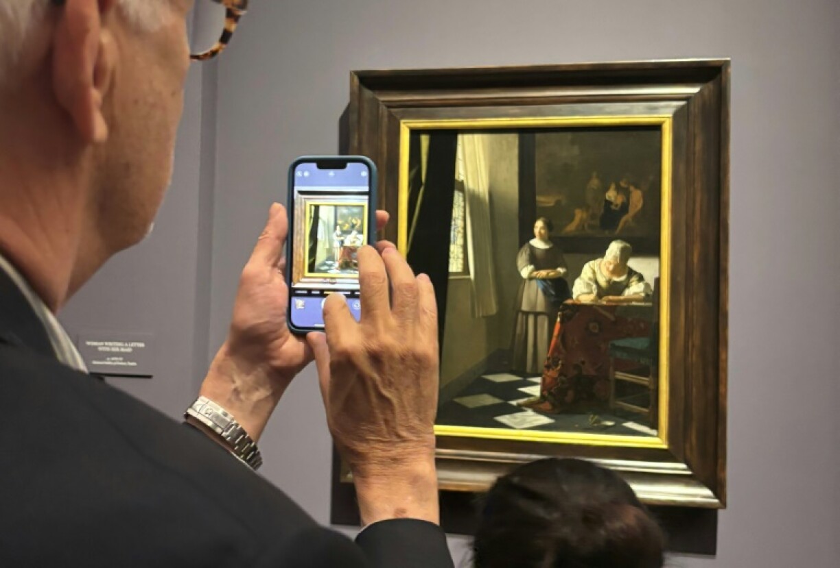 A visitor takes a picture of 'Woman Writing a Letter with her Maid' at the Frick
