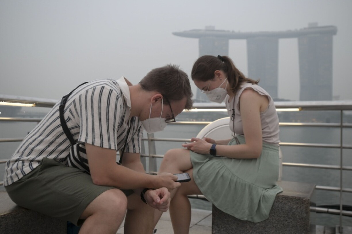 Tourists wear protective masks while seated across Marina Bay Sands in Singapore on October 15, 2026, as the country continues to be shrouded in haze caused by fires in Indonesia